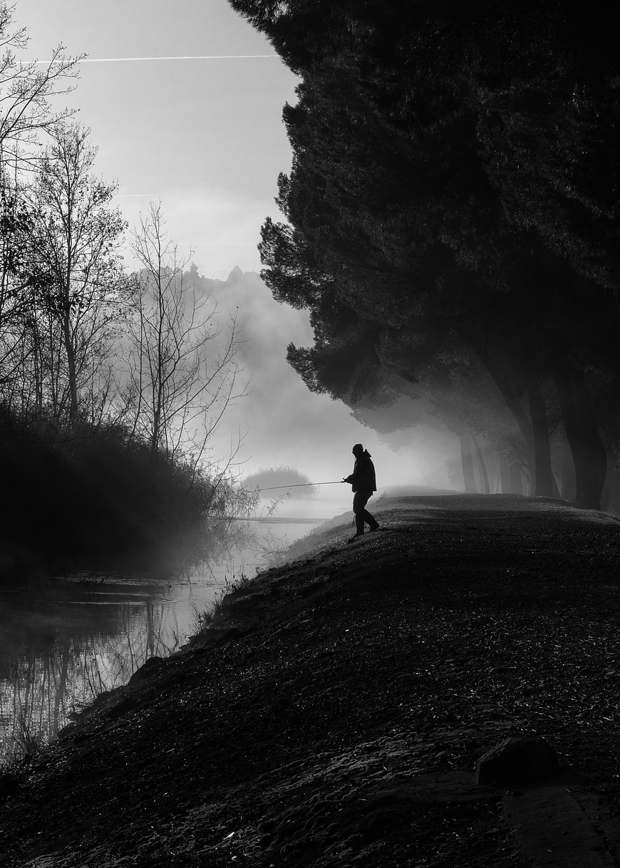 Silhouette of fisherman on misty riverbank in black and white