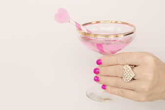 Hand holding gold-rimmed champagne glass with pink drink and heart stirrer