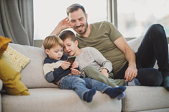Happy father and two sons watching smartphone on couch