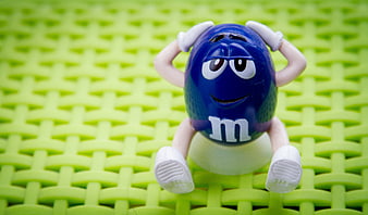 Blue M&M Character Toy Sitting On Green Woven Surface