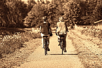 Two women cycling away on a rural path in sepia tone