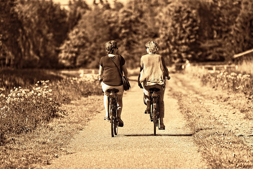 Two women cycling away on a rural path in sepia tone