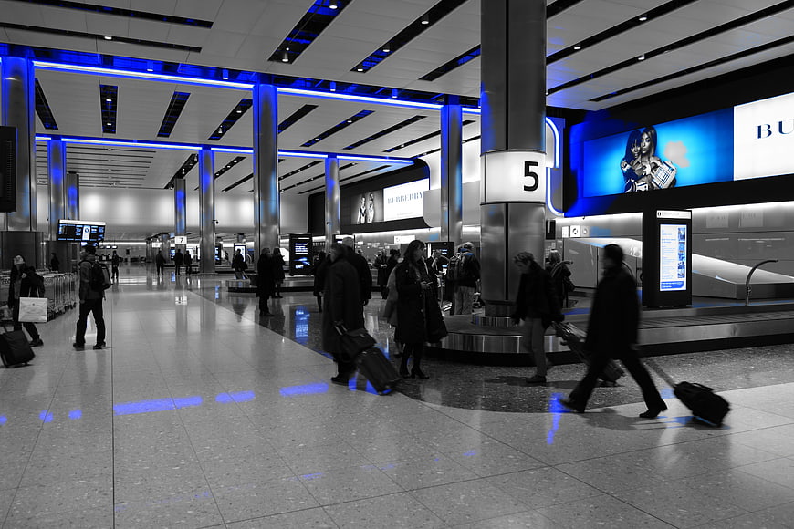 Travelers with luggage in modern airport terminal with blue lighting