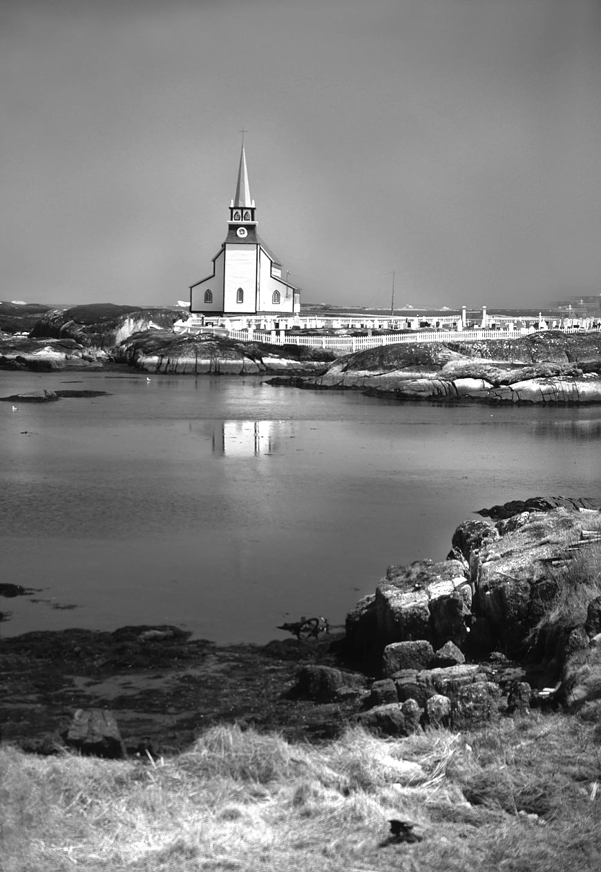 Black and white photo of white church on rocky island