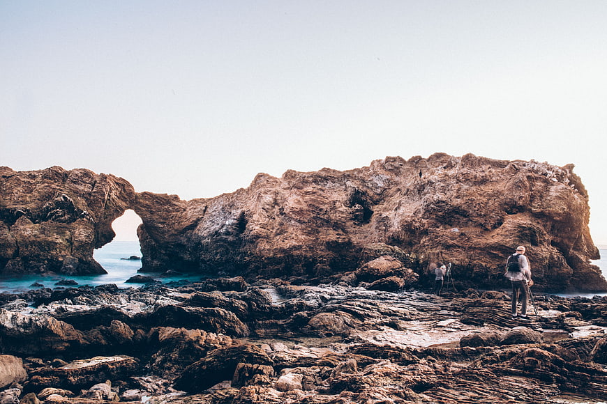 Photographers capturing coastal rock arch formation
