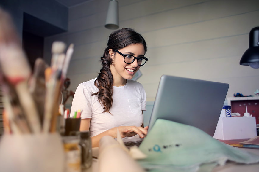 Smiling woman with glasses working on laptop in art studio