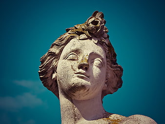 Close-up of weathered stone statue head against blue sky