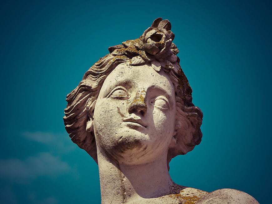 Close-up of weathered stone statue head against blue sky