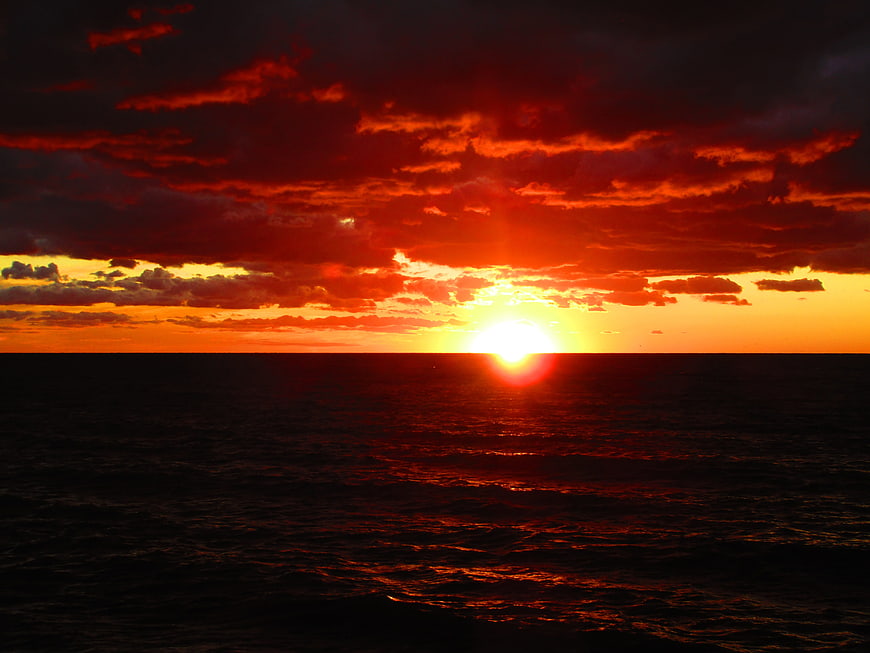 Dramatic fiery red sunset over dark ocean horizon