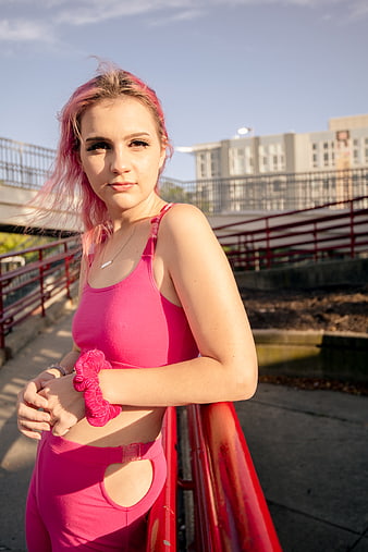 Young woman with pink hair in pink workout gear leaning on railing
