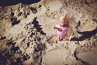 Blonde doll with messy hair buried in sand