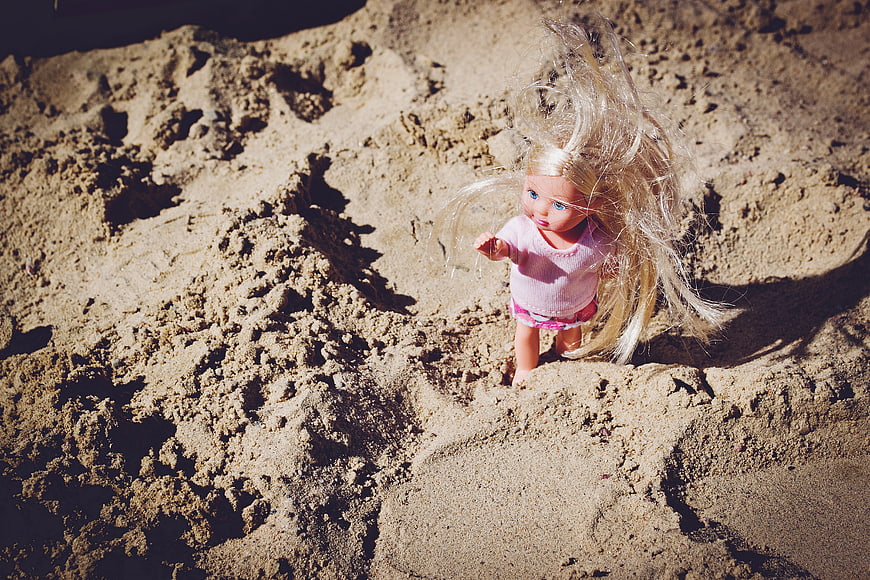 Blonde doll with messy hair buried in sand