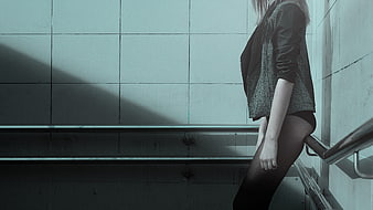 Woman in black stockings and jacket leaning against tiled wall