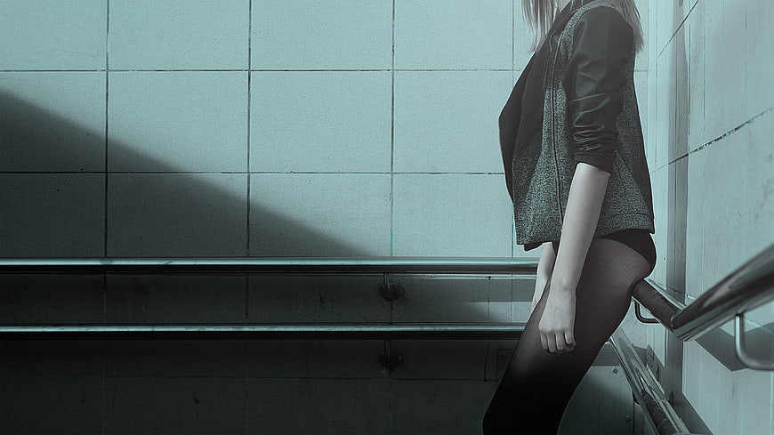 Woman in black stockings and jacket leaning against tiled wall