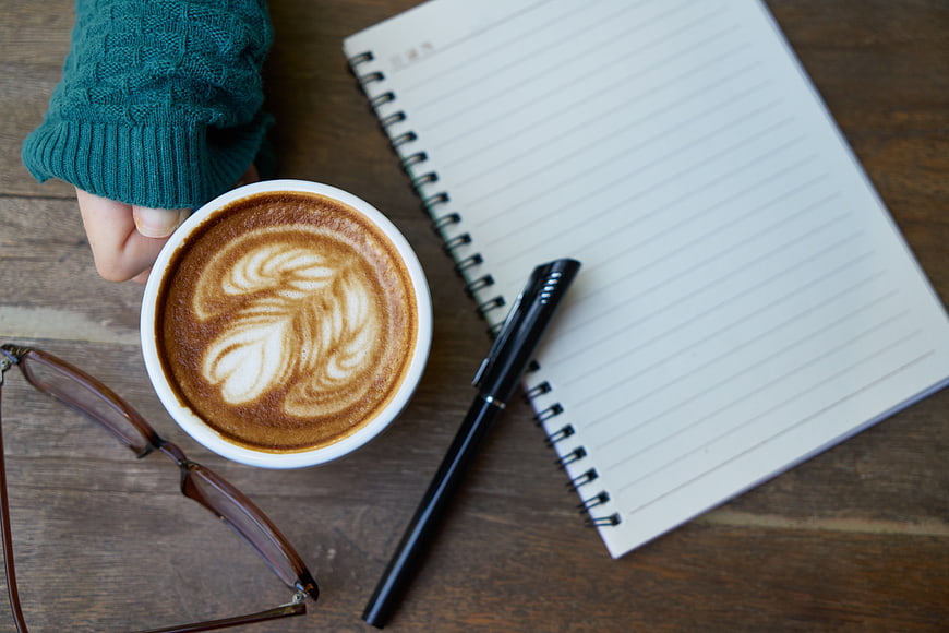 Flat lay of latte art coffee, notebook, and pen on wooden table