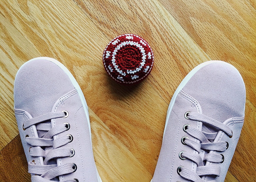 Purple sneakers and red hacky sack on wooden floor