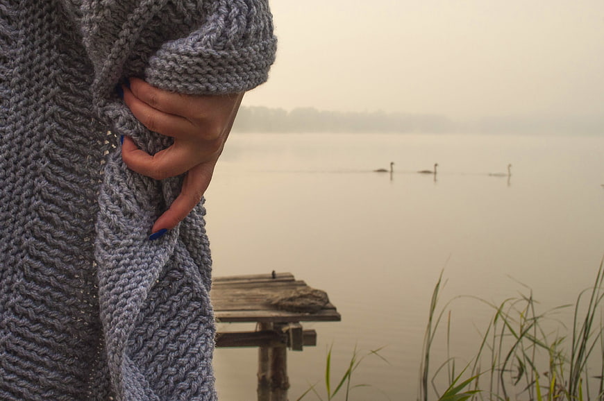 Woman in gray knit sweater by foggy lake with swans