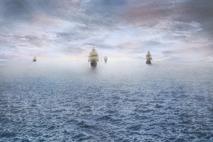 Sailing ships on calm ocean horizon at dawn