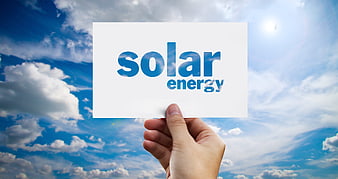 Hand holding solar energy card against blue sky with clouds