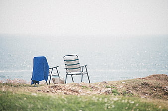 Two empty chairs overlooking the ocean on a grassy cliff