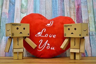 Two cardboard robots holding a red heart plush with Love You text