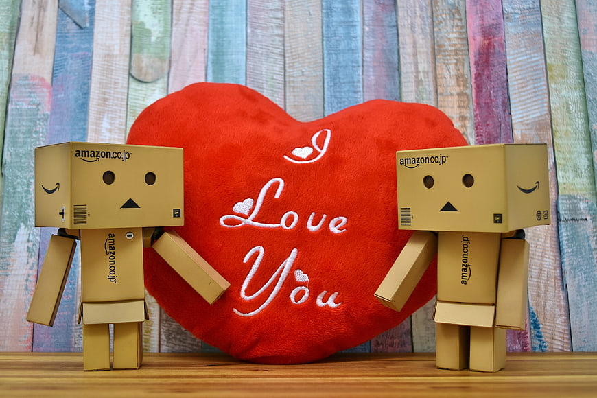 Two cardboard robots holding a red heart plush with Love You text
