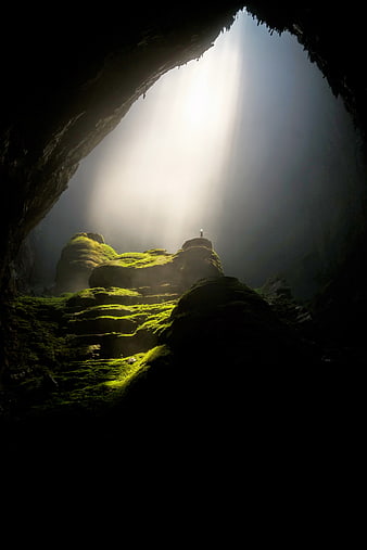 Silhouette of hiker in mossy cave with dramatic sunlight beam