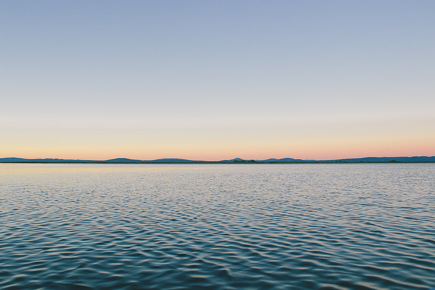 Serene Lake Sunset with Distant Mountains and Calm Water