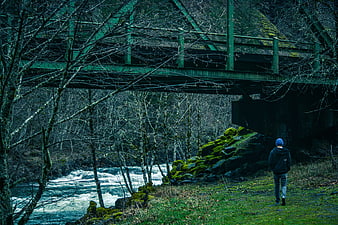 Man Walking Under Green Bridge by River