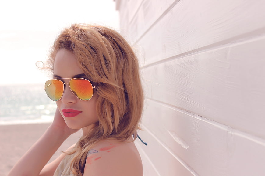 Young Woman Wearing Reflective Sunglasses Leaning Against White Wall