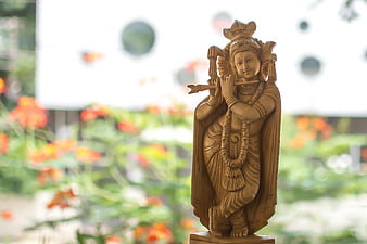 Wooden Krishna Statue Playing Flute With Blurred Garden Background