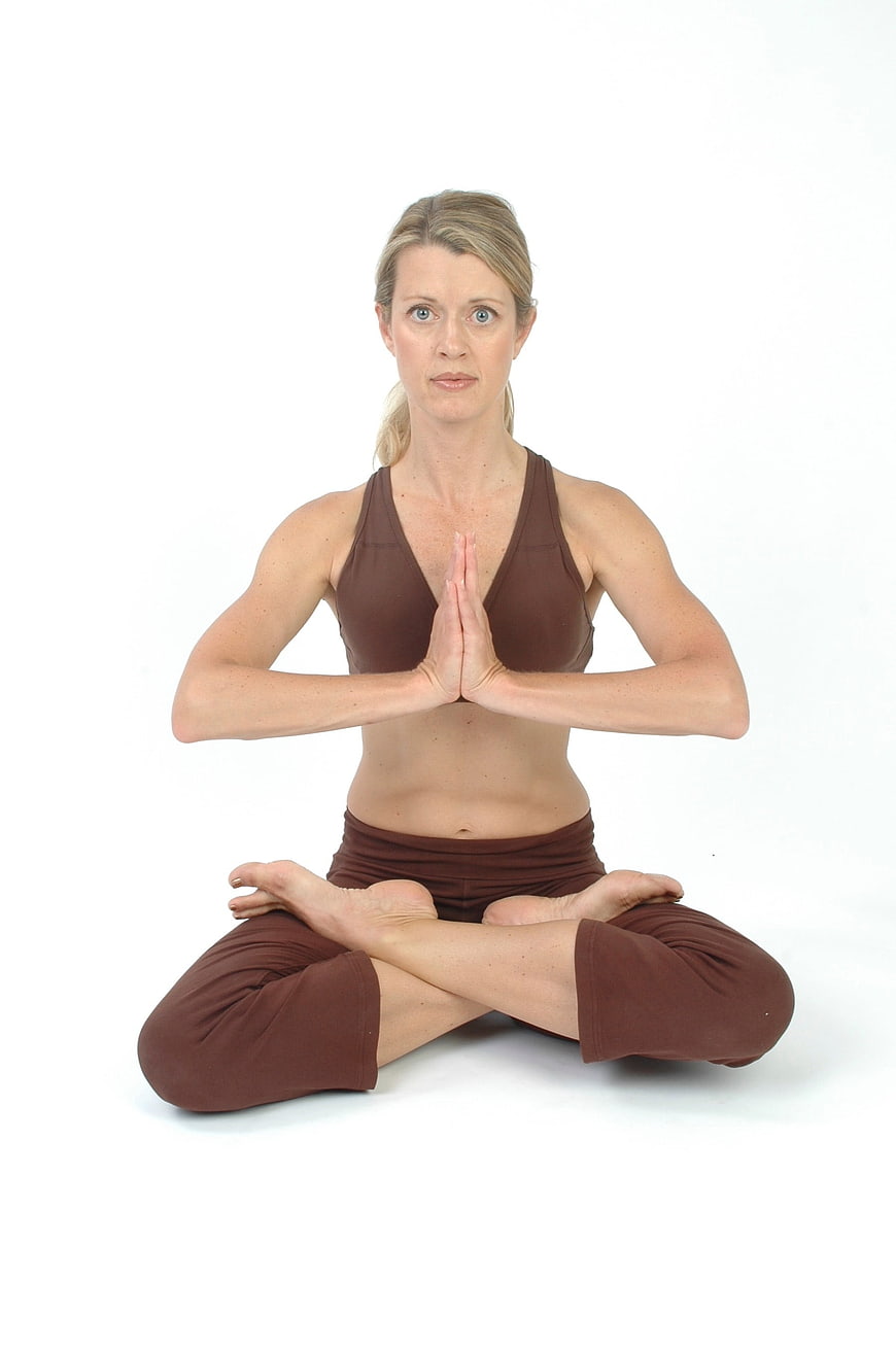 Woman in lotus yoga pose with hands in prayer position on white background