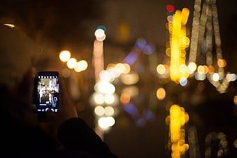 Person taking photo of bokeh lights with smartphone at night