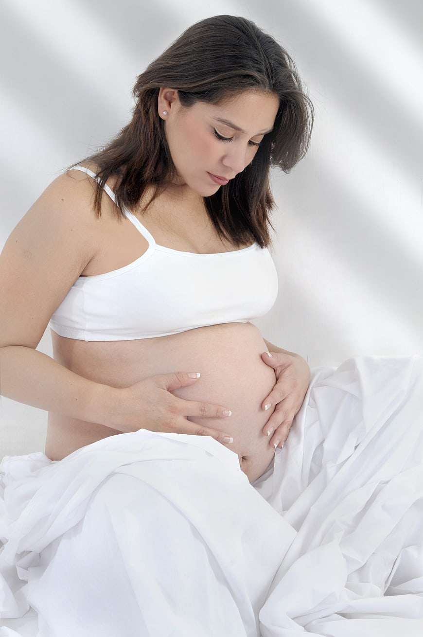 Pregnant woman cradling belly in white studio setting