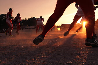 Low-Angle Action Shot of Soccer Players Running on a Dusty Field at Sunset