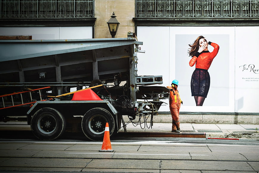 Construction worker standing near truck and fashion billboard