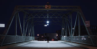 Lone Figure Walking on Steel Bridge at Night