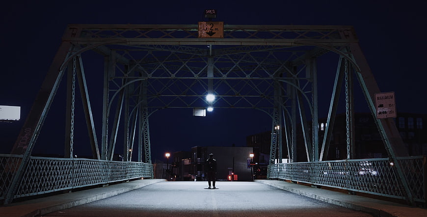 Lone Figure Walking on Steel Bridge at Night