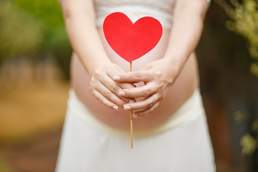 Pregnant woman holding red heart over belly