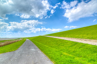 Paved path along a green Dutch dike under blue sky