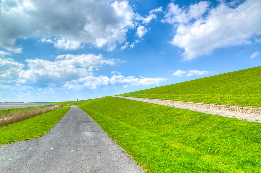 Paved path along a green Dutch dike under blue sky