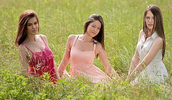 Three young women in dresses sitting in a green meadow