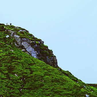 Hikers on a lush green mountain ridge against a clear sky