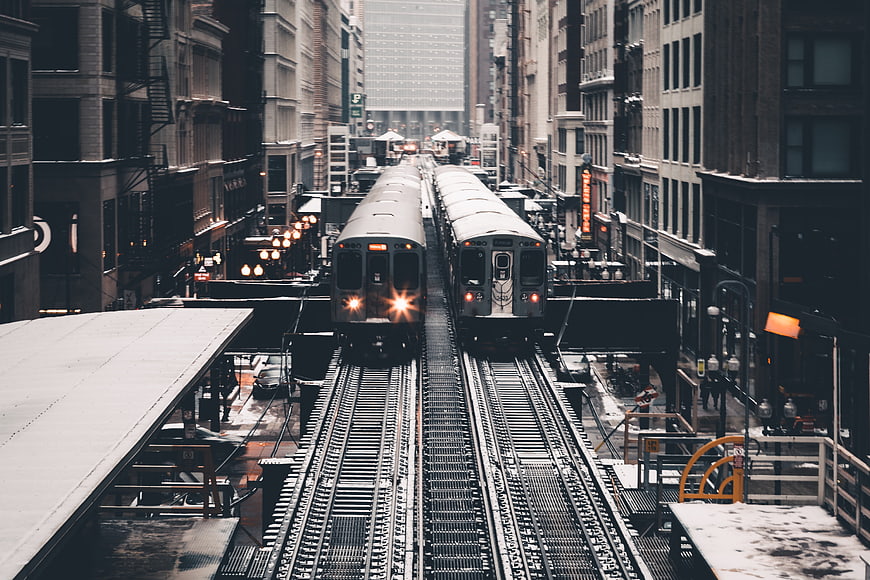 Two elevated trains on parallel tracks in a snowy city