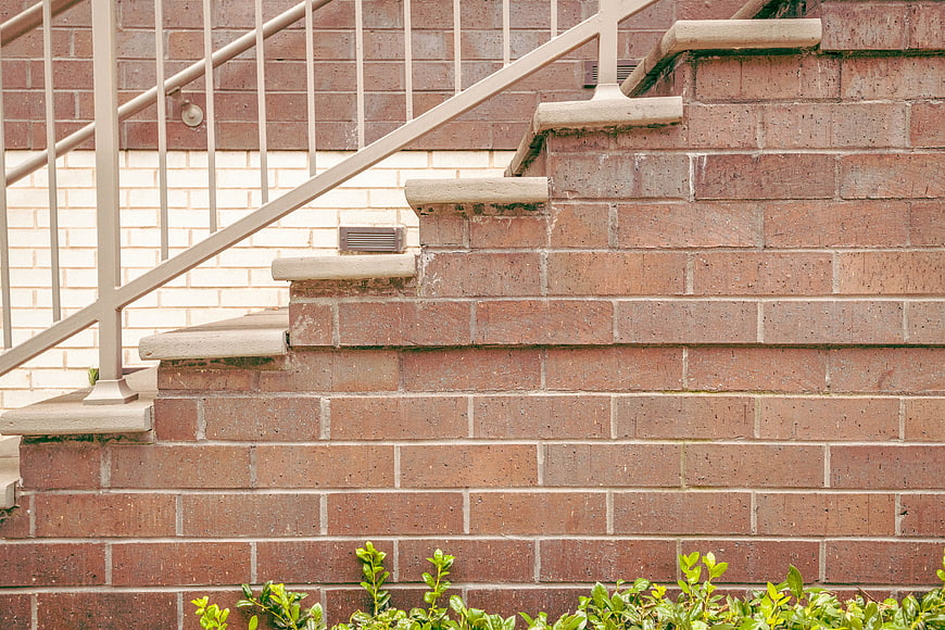 Red brick stairs with metal railing and green plants