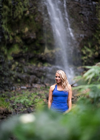 Blonde woman in blue tank top standing near waterfall