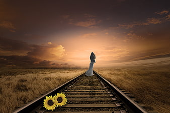 Woman walking away on railway tracks at sunset with sunflowers