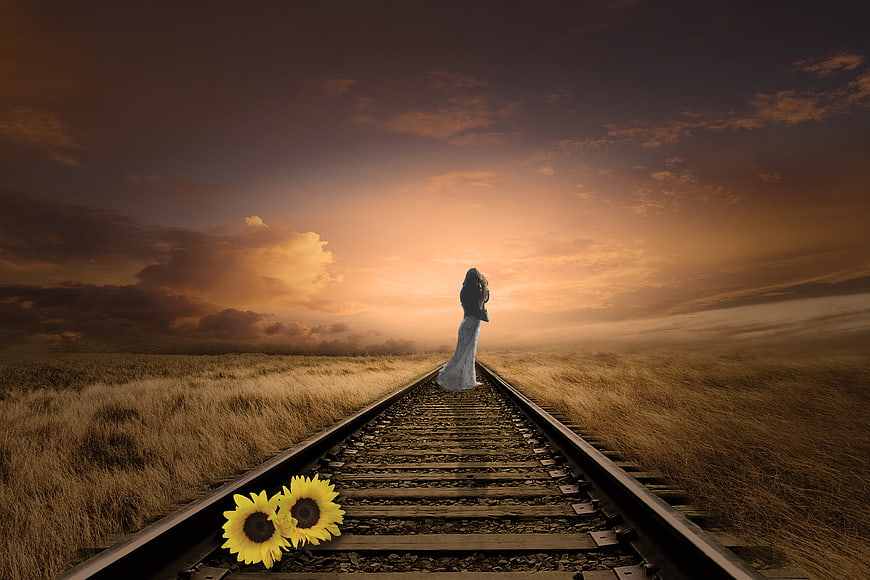 Woman walking away on railway tracks at sunset with sunflowers