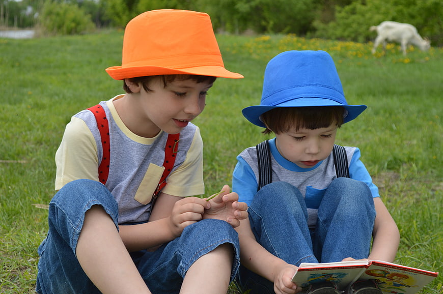 Two young boys reading a book in a grassy meadow