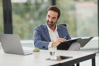 Happy businessman writing on clipboard at office desk